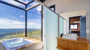 A modern bathroom with a large window, a wooden vanity, a bathtub, and a mirror.