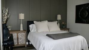 A bedroom with a large bed, two bedside tables, a nightstand, a decorative vase, and a wall-mounted artwork. - Roll Mill, Steel Bend Guest Houses: Roll Mill (Osceola)
