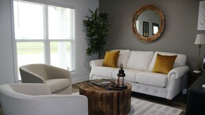 A living room with a white sofa, a round wooden coffee table, and a white armchair. - Roll Mill, Steel Bend Guest Houses: Roll Mill (Osceola)