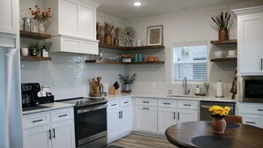 A modern kitchen with white cabinets, a central island, and a dining table. - Roll Mill, Steel Bend Guest Houses: Roll Mill (Osceola)