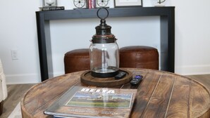 A round wooden table with a glass lantern, a remote control, and a travel magazine titled "Delta Cities." - Roll Mill, Steel Bend Guest Houses: Roll Mill (Osceola)