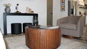 Ein modernes Wohnzimmer mit einem runden Holztisch, einem grauen Sessel und einer schwarzen Konsole mit Dekoration.