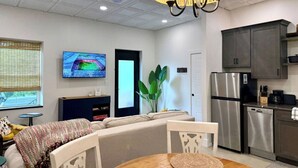 A modern living room with a sofa, a dining table, and a kitchen area with a refrigerator and cabinets.