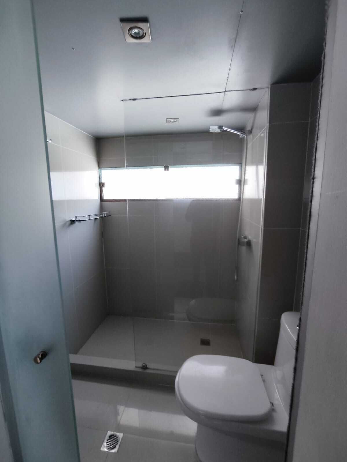 Un baño pequeño y moderno con cabina de ducha de vidrio, inodoro y ventana que proporciona luz natural.