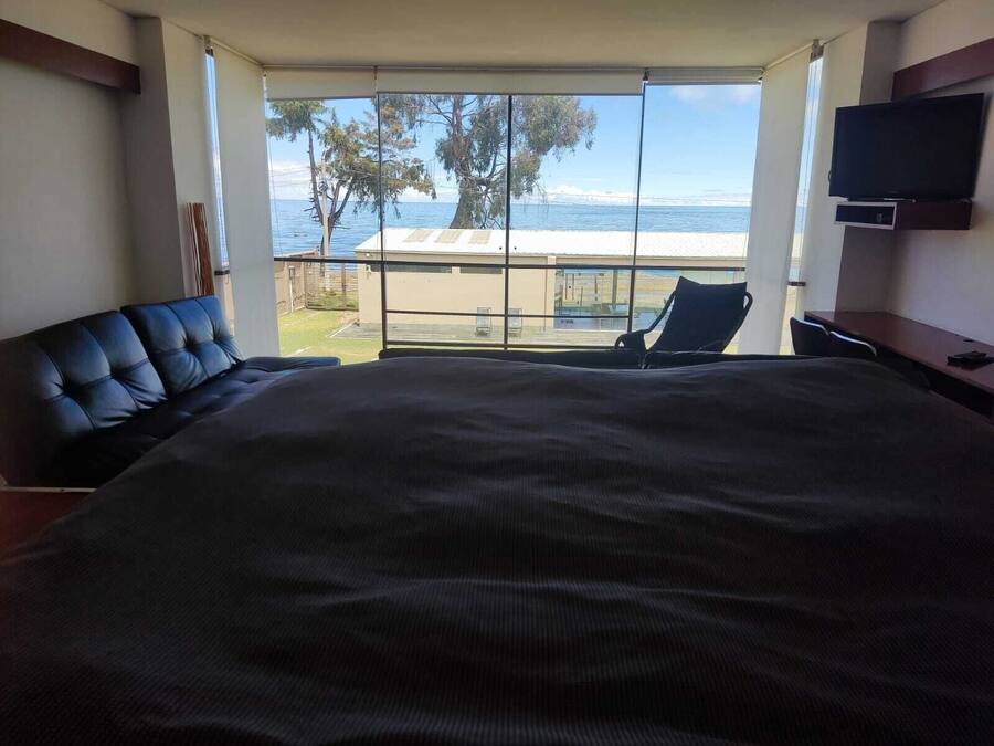A bedroom with a large bed, a TV, and a balcony with a view of the sea.