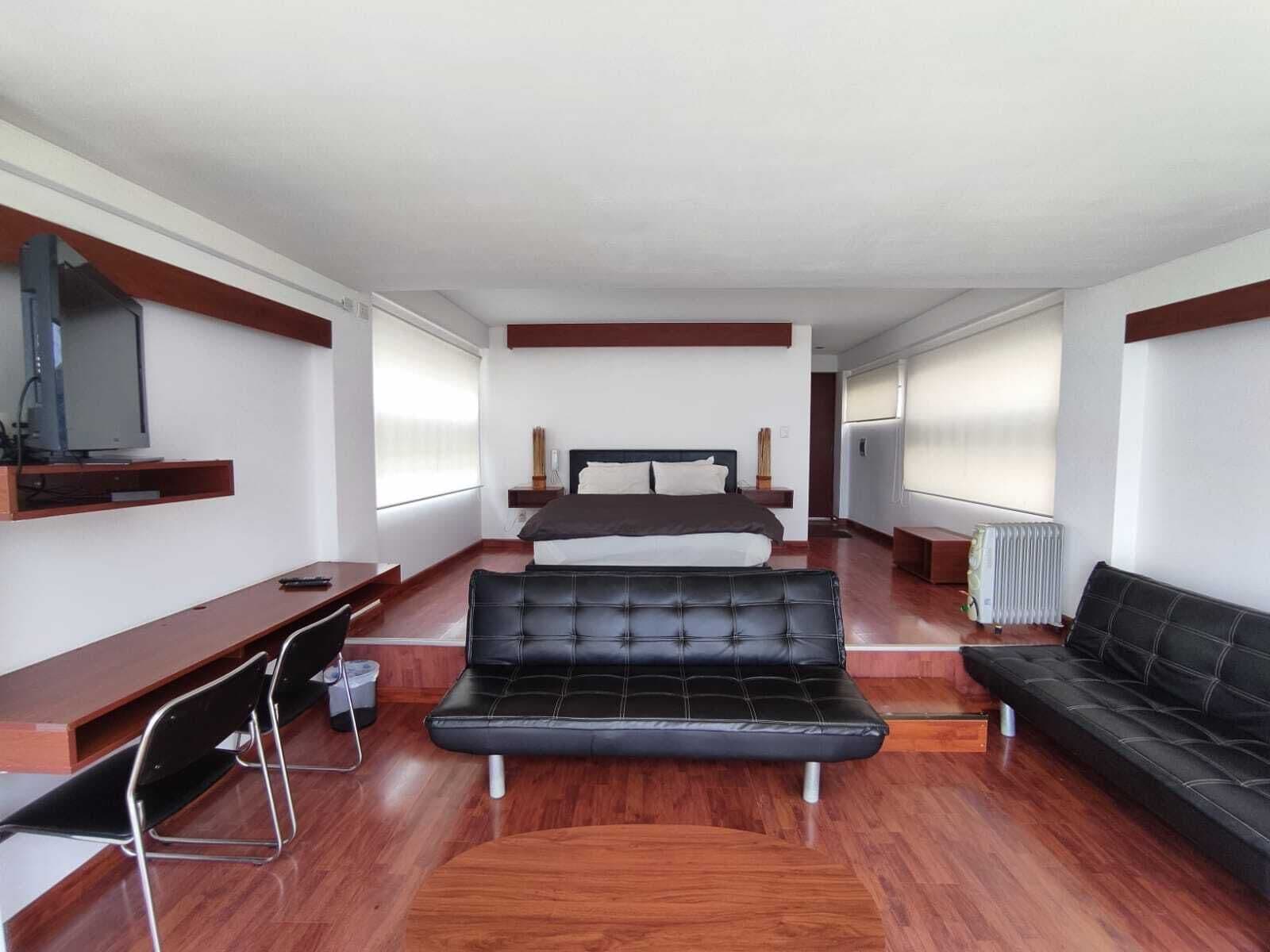 A modern hotel room with a bed, a sofa, a desk, and a television.