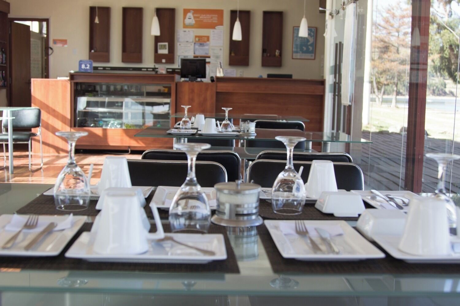 A restaurant with tables set for dining, a counter with a display case, and a view of the outdoors.