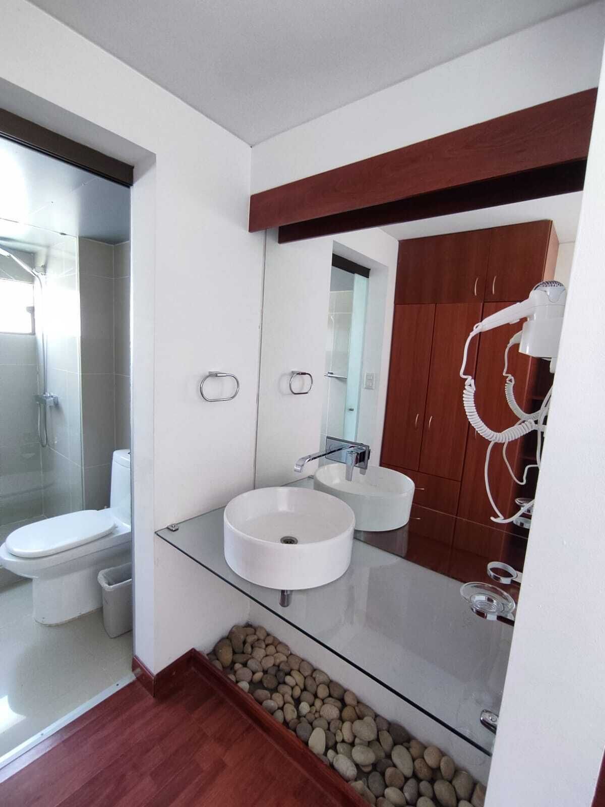 Un baño moderno con lavamanos de vidrio, inodoro y zona de ducha.