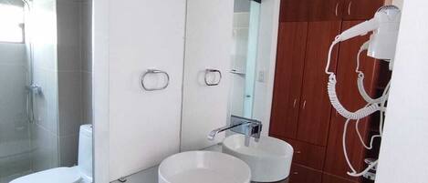 Un baño moderno con lavamanos de vidrio, inodoro y zona de ducha.