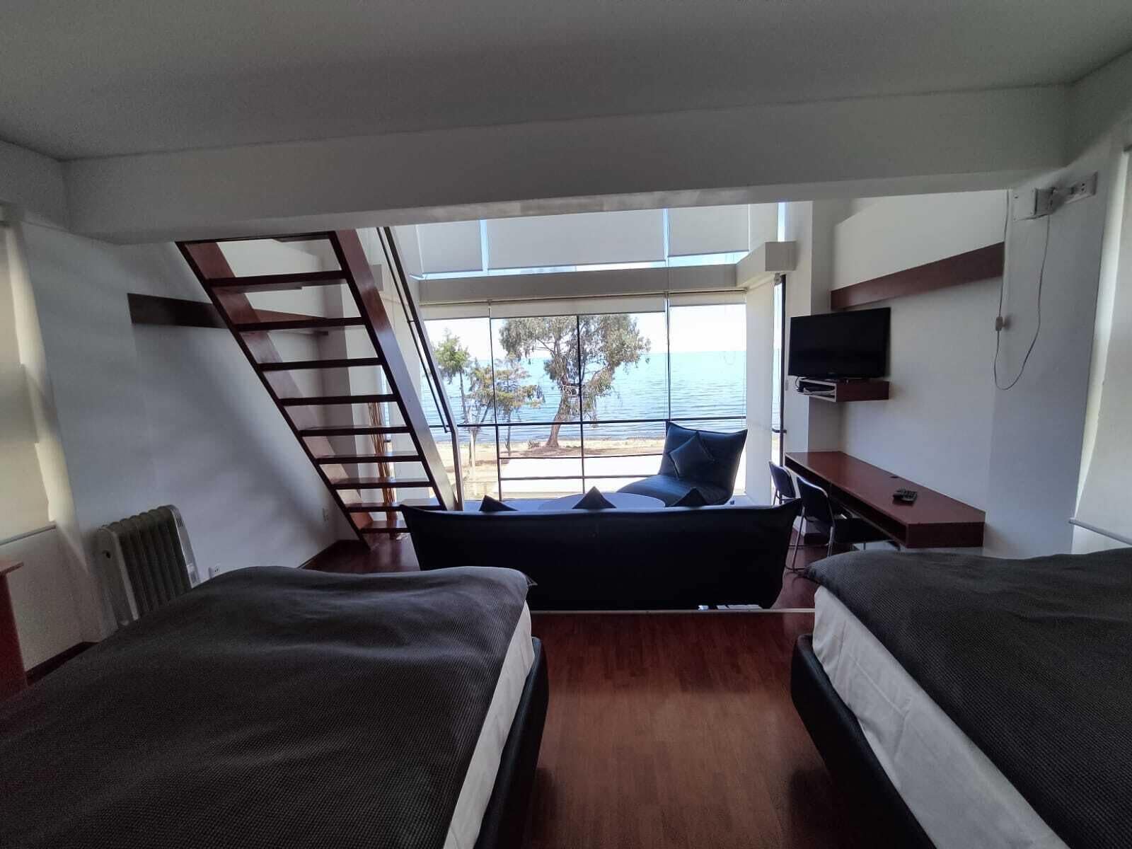 A bedroom with two beds, a TV, and a view of the sea.