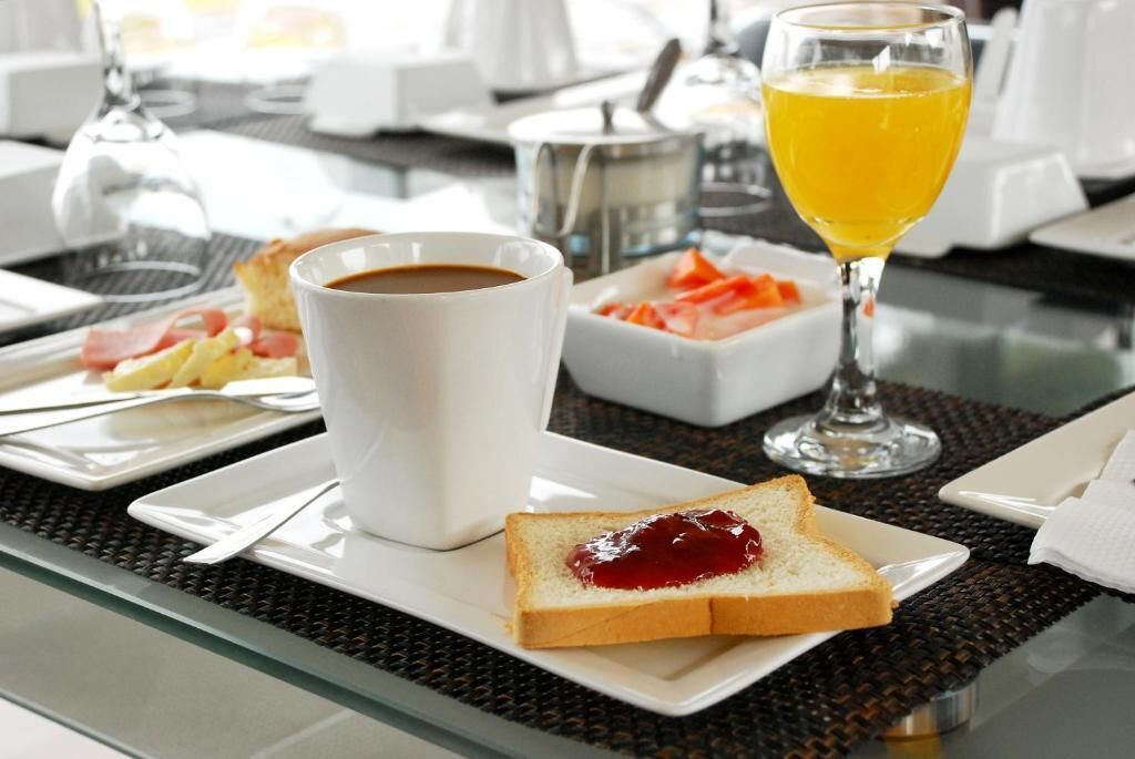Un desayuno con una taza de café, un vaso de jugo de naranja, tostadas con mermelada y un plato de huevos con tocino.