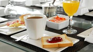 Un desayuno con una taza de café, un vaso de jugo de naranja, tostadas con mermelada y un plato de huevos con tocino.
