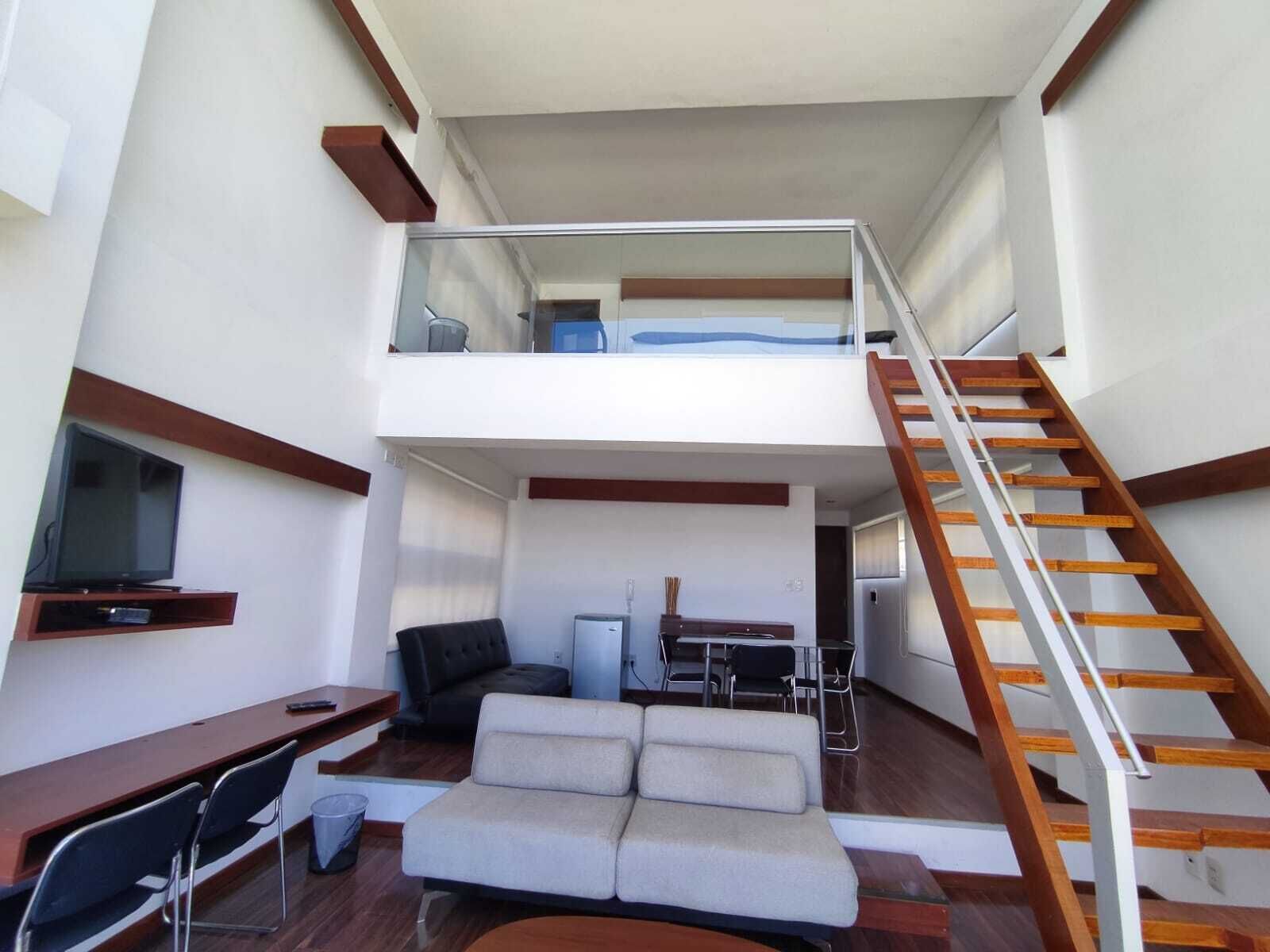A modern interior with a loft-style living area, a dining space, and a staircase.