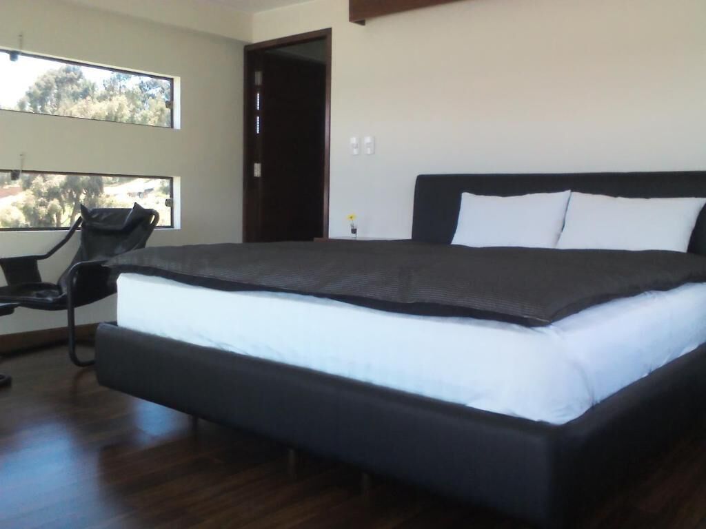 A modern bedroom with a large bed, a chair, and a view of the outdoors through a window.