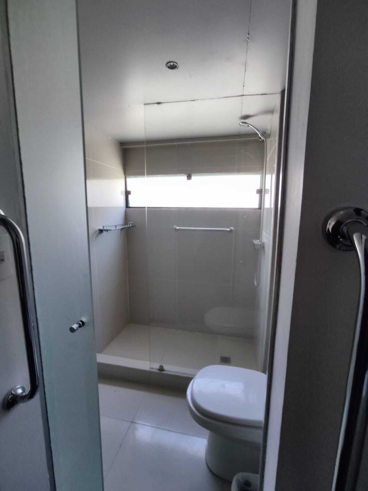 Un baño pequeño y cerrado con cabina de ducha de vidrio, inodoro y barra de apoyo metálica.