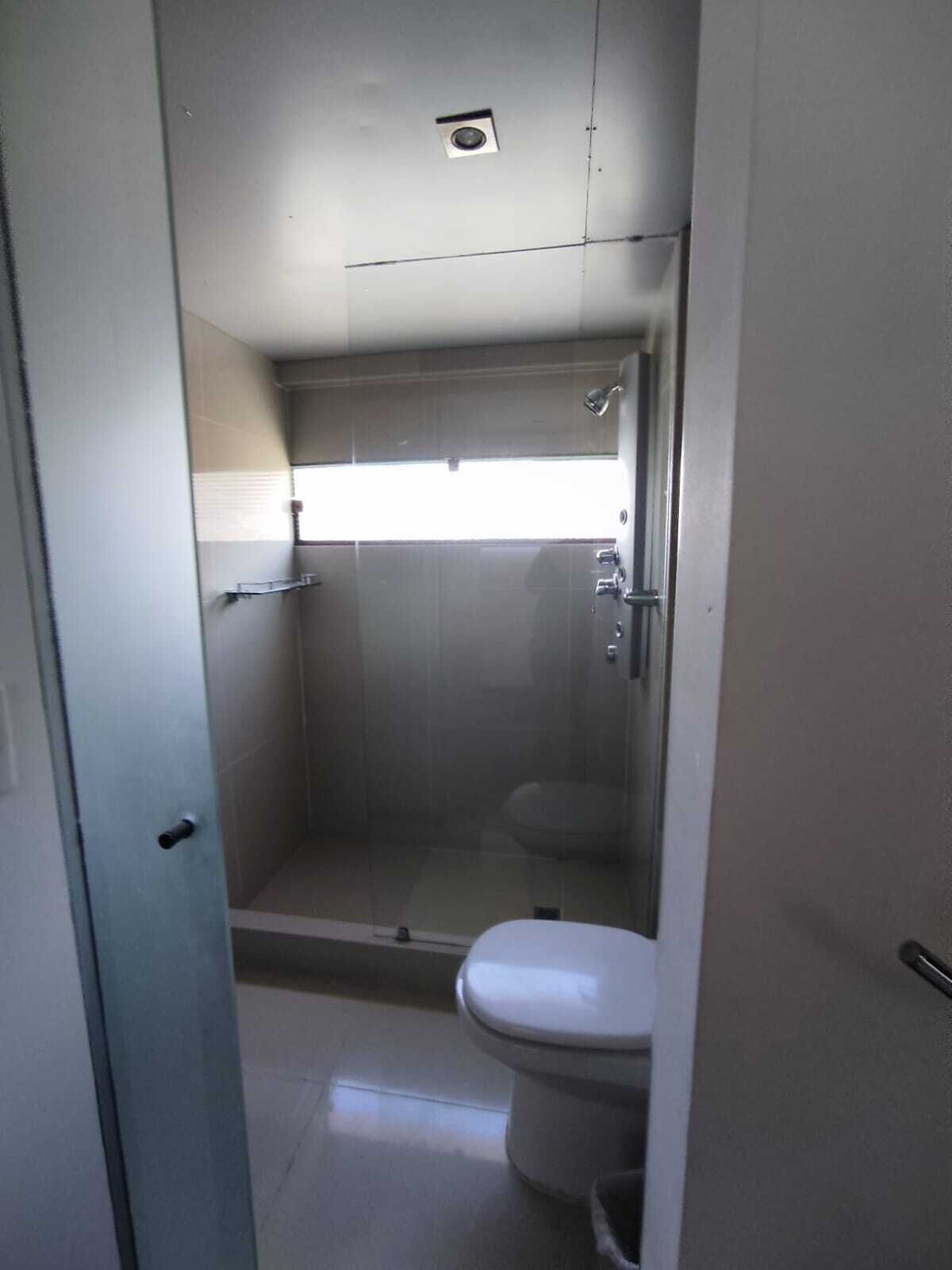A small, enclosed bathroom with a toilet, a shower stall, and a window providing natural light.