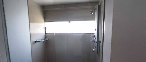 A small, enclosed bathroom with a toilet, a shower stall, and a window providing natural light.