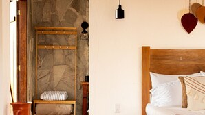Un dormitorio con pared de piedra, una cama de madera, una lámpara colgante y un estante en la pared.