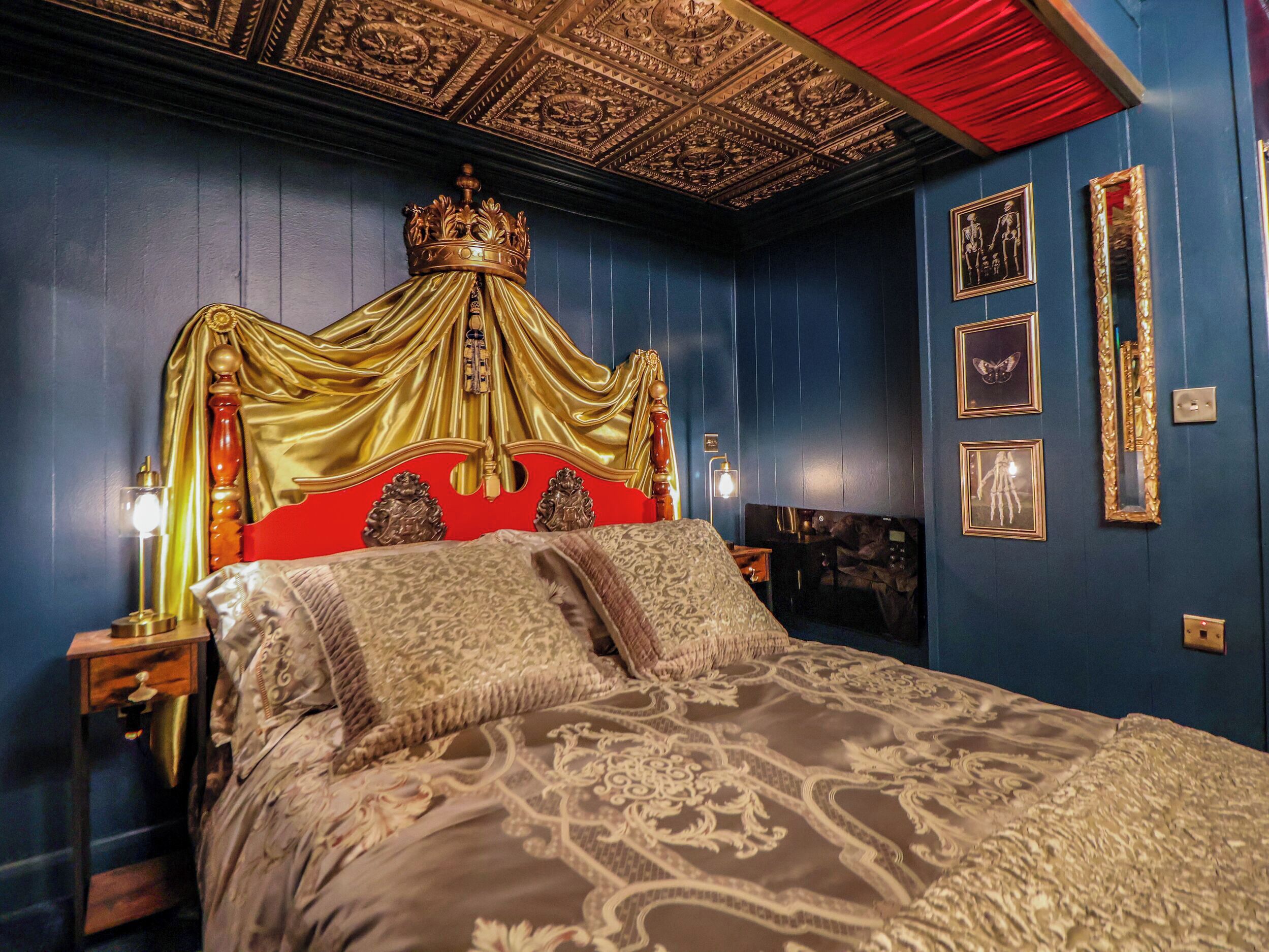 Een luxe slaapkamer met een gouden hemelbed, versierd plafond en omlijste kunstwerken aan de muur.