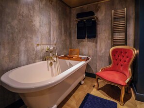 A bathroom with a freestanding bathtub, a red upholstered chair, and a towel rack. - The Hollow (Holywell)