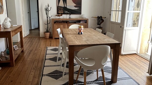 A dining area with a wooden table, white chairs, a hanging light fixture, and a poster on the wall. - Charming house with swimming pool (Bordeaux)