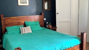 A bedroom with a wooden bed, teal bedding, a framed picture, a mirror, and a white door. - Charming house with swimming pool (Bordeaux)