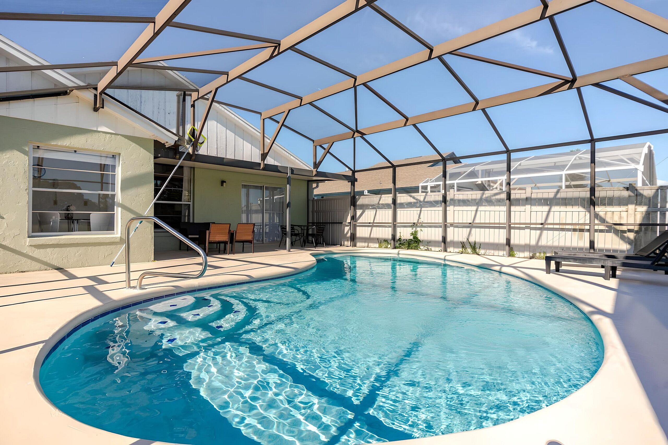 Una piscina interior con agua cristalina y azul, rodeada por una zona cubierta con estructura metálica y paneles de vidrio.