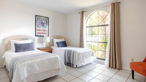 Habitación de hotel con dos camas, un ventanal con cortinas, un cuadro enmarcado en la pared y una silla roja.
