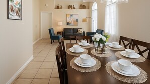 Un coin repas avec une table ronde dressée pour six personnes, entourée de chaises. On aperçoit un canapé et une petite table d’appoint au fond.