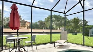 A covered outdoor area with a pool, chairs, and a table.