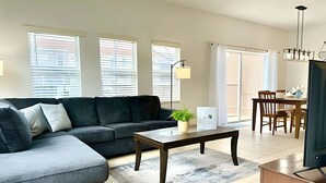 A modern living room with a sectional sofa, a coffee table, and a dining area with a table and chairs.