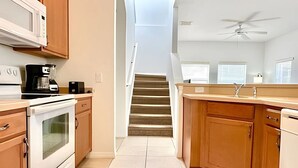 A kitchen with wooden cabinets, a white stove, a microwave, and a ceiling fan.