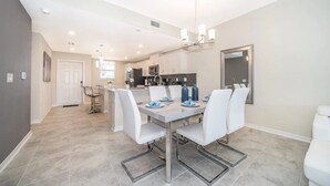 Une cuisine moderne avec des meubles blancs, un îlot central et un coin repas comprenant une table et des chaises.