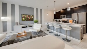 A modern kitchen with a central island, bar stools, and a flat-screen TV mounted on the wall.