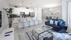 A modern living room with a sofa, coffee table, and a dining area in the background. - 4BR Townhome | Private Pool | 10 min to Disney (Kissimmee)