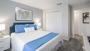 A bedroom with a bed, nightstands, a dresser, and a door. - 4BR Townhome | Private Pool | 10 min to Disney (Kissimmee)