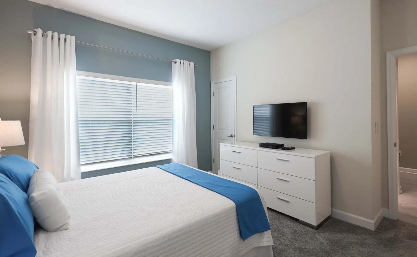 A bedroom with a bed, a dresser, a television, and a window with curtains.