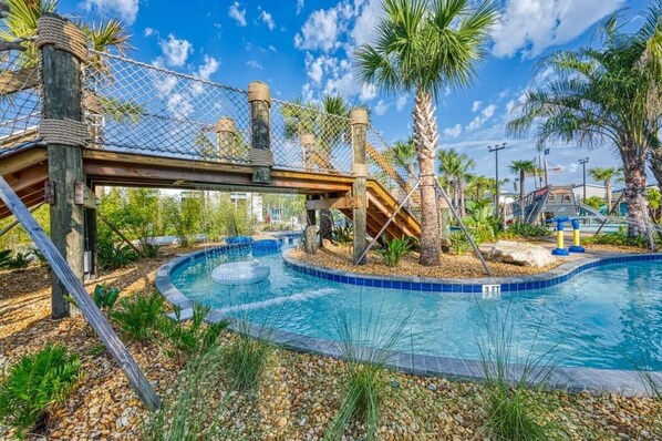 Une piscine avec un pont en bois, des palmiers et un ciel bleu azur.