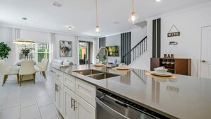 Una cocina moderna con una isla grande, electrodomésticos de acero inoxidable y un comedor con sillas blancas.
