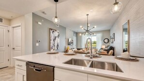 Una cocina moderna con una isla central, pileta de acero inoxidable e iluminación colgante.