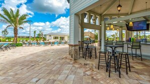 A covered outdoor area with poolside chairs, a bar area with stools, and a large TV screen. - 3BR/2BA Apartment – 10 Min to Disney Parks! (Kissimmee)