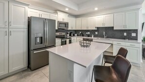 A modern kitchen with white cabinetry, stainless steel appliances, and a central island with chairs. - 3BR/2BA Apartment – 10 Min to Disney Parks! (Kissimmee)