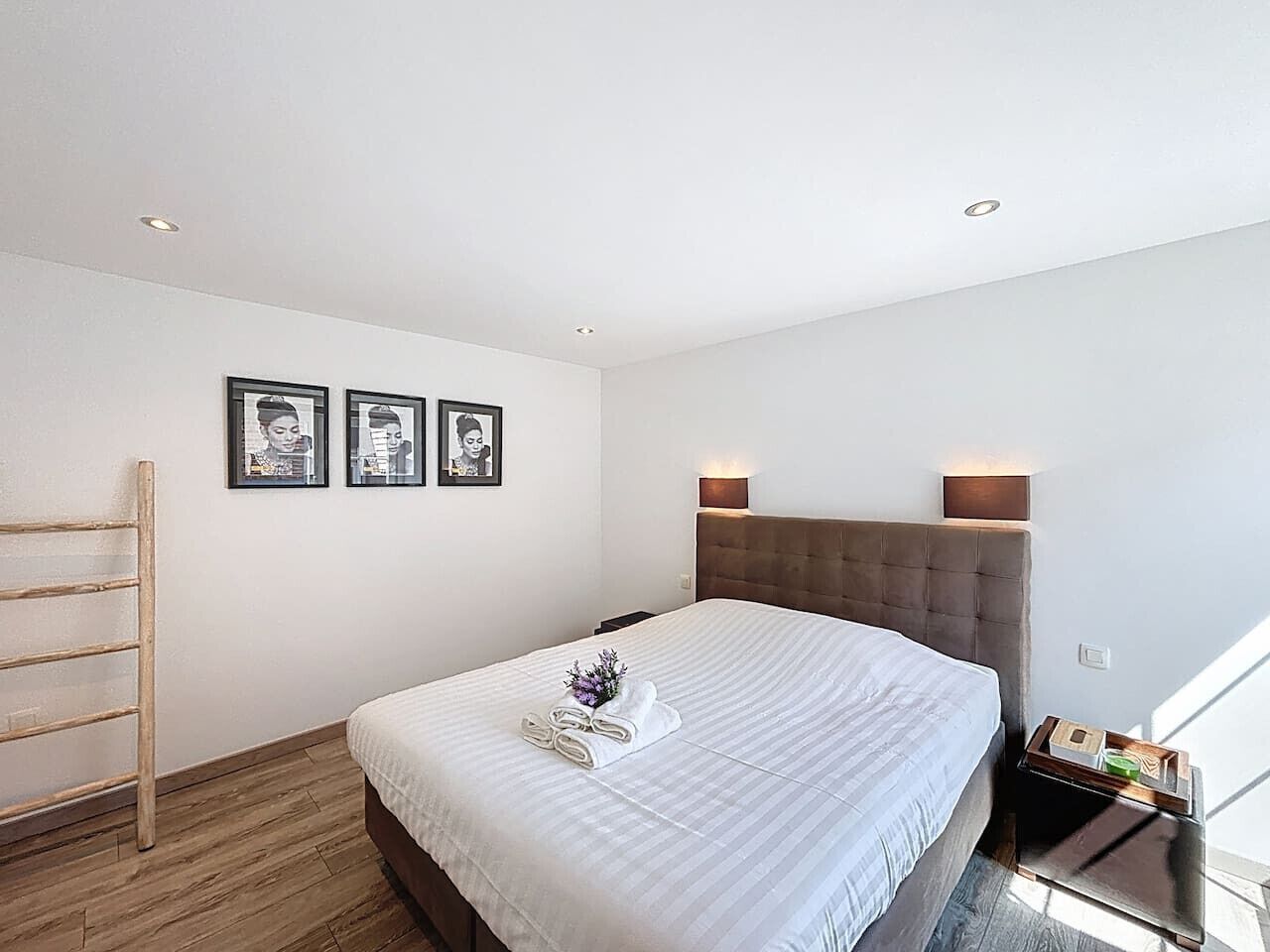 A modern hotel room with a large bed, a wooden ladder, and three framed pictures on the wall.