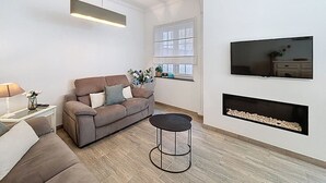 A modern living room with a sofa, a coffee table, a TV mounted on the wall, and a fireplace. - Maison 't Blyhuis - De Panne (De Panne)