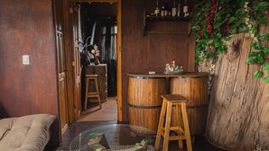 A cozy room with a wooden floor, a glass table, a bench, and a bar area with wooden barrels. - Casita Del Arbol Trini By GEstores (Omitlán de Juárez)