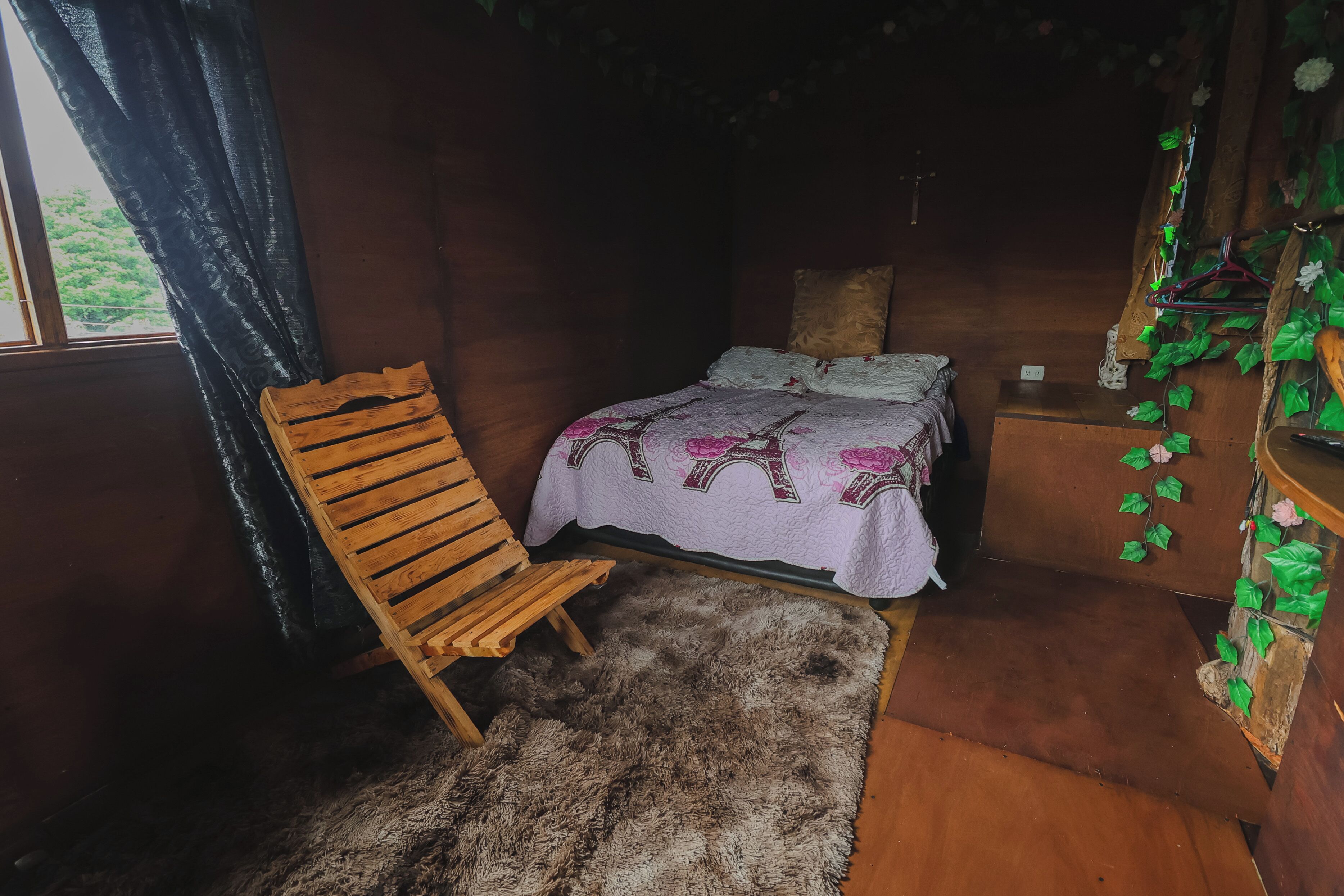 Una habitación con una cama, una silla de madera, un felpudo de piel y un aparador de madera con plantas.