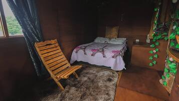 Una habitación con una cama, una silla de madera, un felpudo de piel y un aparador de madera con plantas.