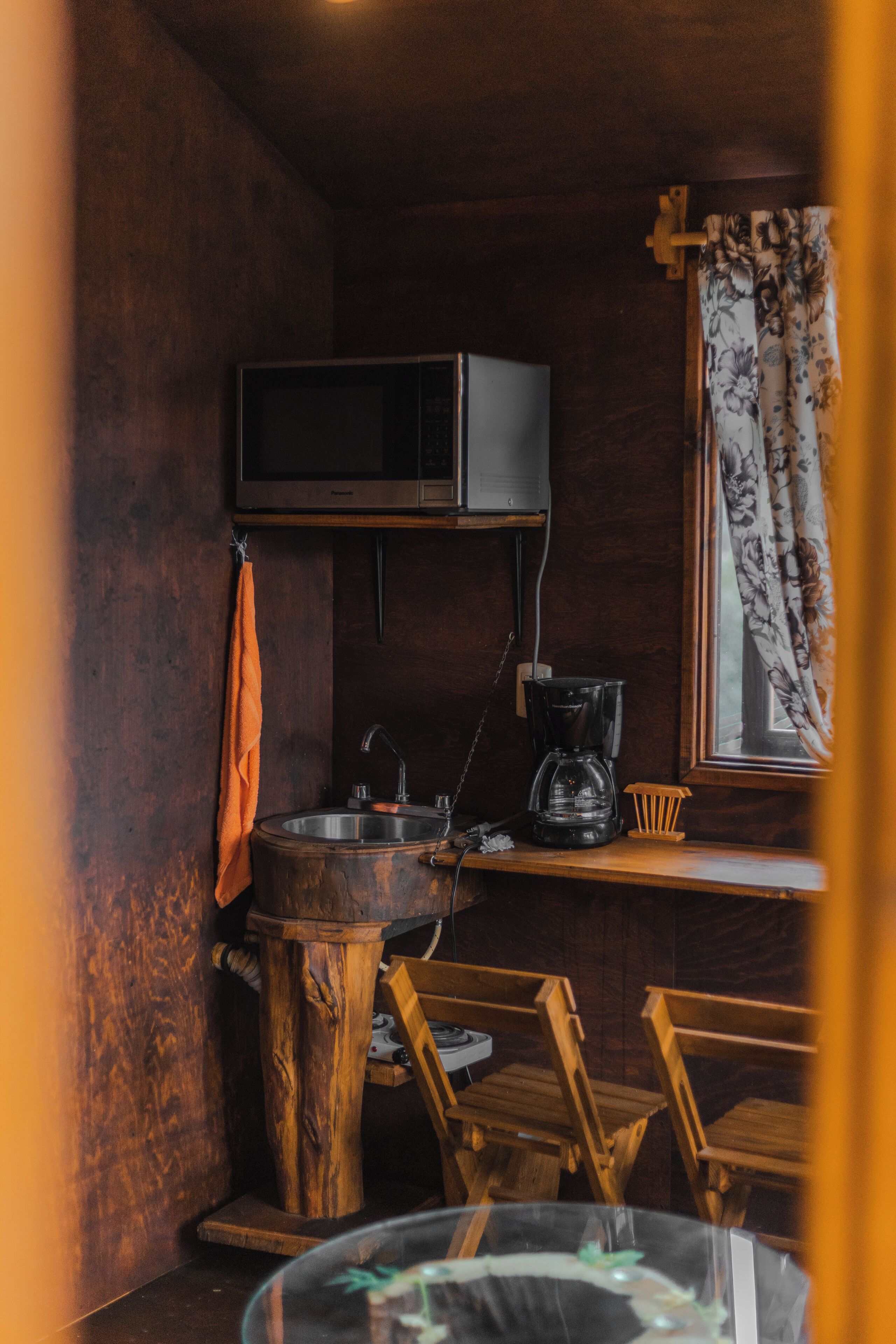 Una cocina rústica con un lavamanos de madera, una cafetera y un televisor fijado en la pared.