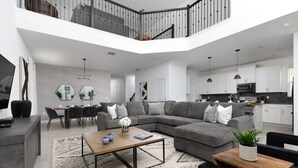 A modern living room with a sectional sofa, a coffee table, and a dining area with a table and chairs. - 5BR/5BA Villa w/ Pool Near Disney (Kissimmee)