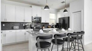 A modern kitchen with white cabinets, stainless steel appliances, and a central island with bar stools. - 5BR/5BA Villa w/ Pool Near Disney (Kissimmee)